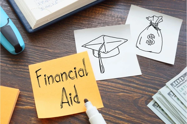 The image shows sticky notes with "Financial Aid" written on one and drawings of a graduation cap and a money bag on the others, along with cash and a pen on a wooden surface.