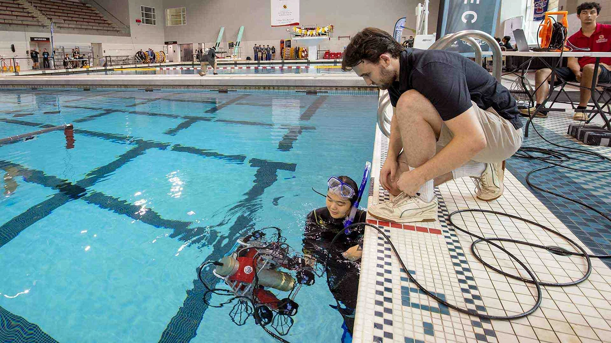 Robotics @ Maryland President and Software Lead Josh Smith watches the Terp team’s robot, Qubo, during testing for the 25th RoboSub competition at the Eppley Recreation Center on Friday. Lt. Hannah Lee, one of the Navy Reserve members on hand to help during the event, treads in the pool.