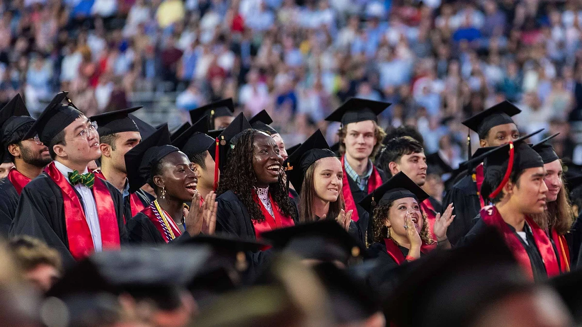 A group of graduates in caps and gowns enthusiastically celebrate at a commencement ceremony.
